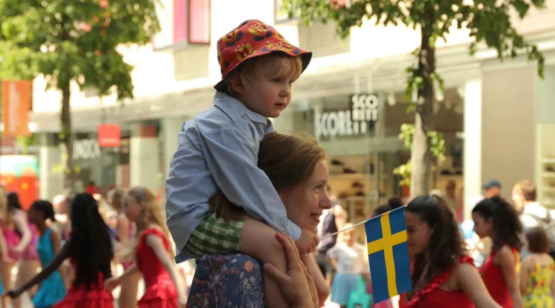 Little boy on his mothers shoulders, holding the Swedish flag among crowd